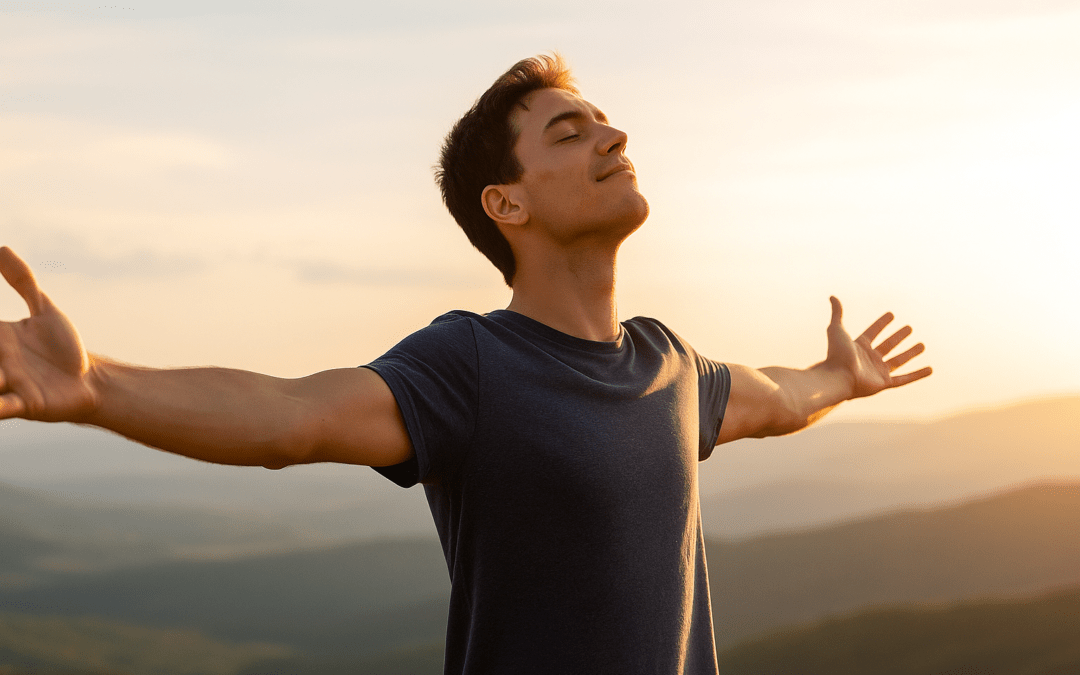 Hombre joven con los brazos abiertos disfrutando del atardecer en la cima de una colina, simbolizando libertad y crecimiento personal.